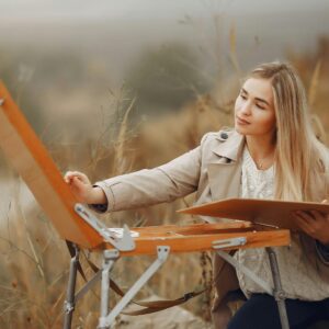 Young woman painting outdoors in an autumn setting, capturing creativity and tranquility.